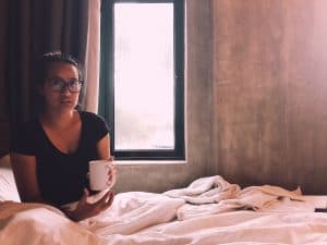 An introverted girl sitting on the bed with a cup of coffee