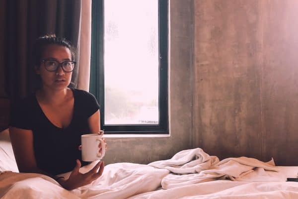 An introverted girl sitting on the bed with a cup of coffee